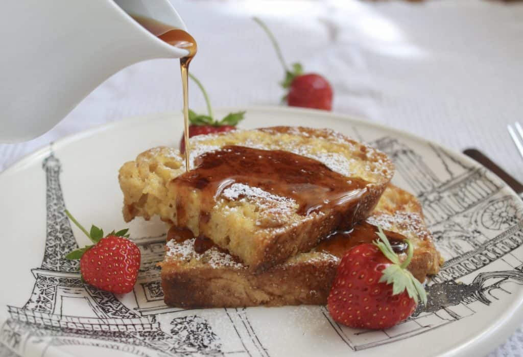 maple syrup being poured over slices of French toast on a plate with berries