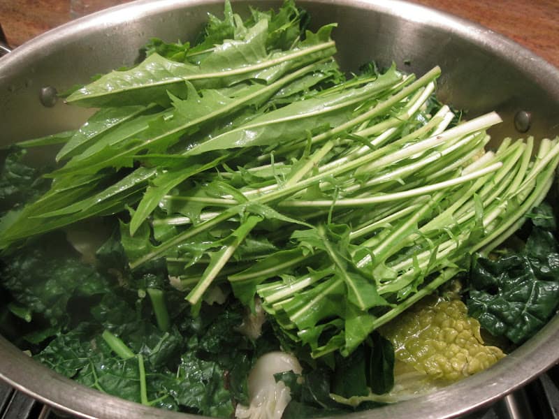 dandelion greens being added to a pan