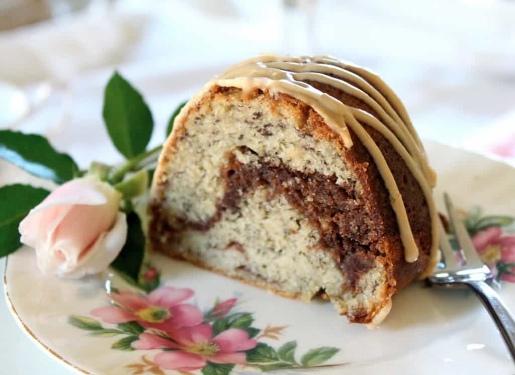 slice of banana and nutella cake on a floral china plate with a rose bud on the side