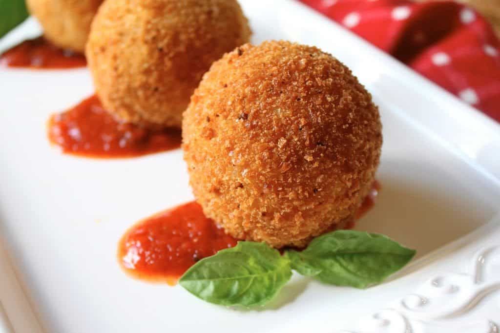 Arancini/Sicilian Rice Balls on a white platter with a little sauce and two basil leaves