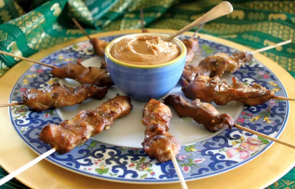 Singapore Chicken Satay skewers on a plate with a bowl of peanut sauce.