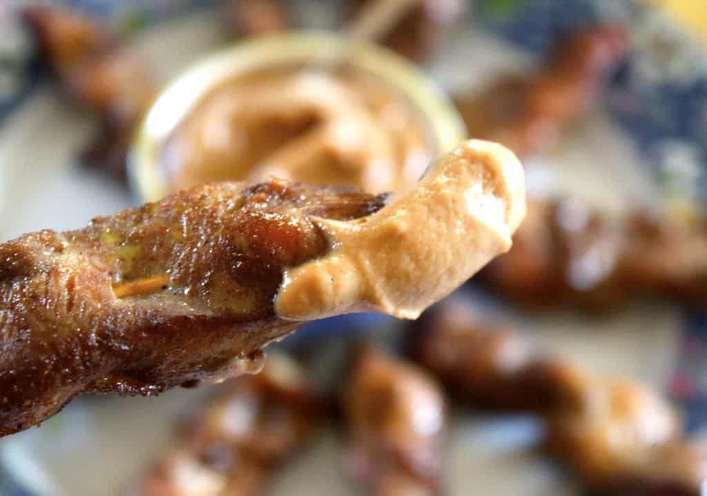 Photo of close up chicken skewered dipped into peanut sauce.