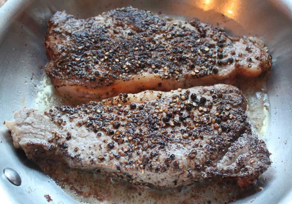 steaks in a pan coated with crushed peppercorns