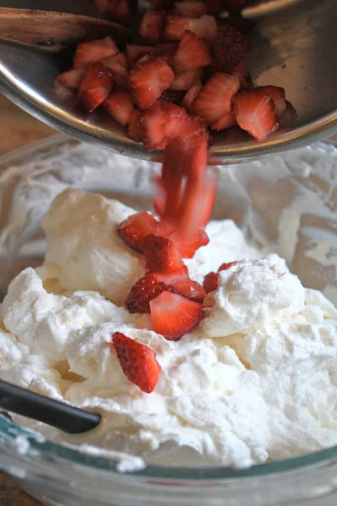 adding strawberries to bowl of cream and yogurt