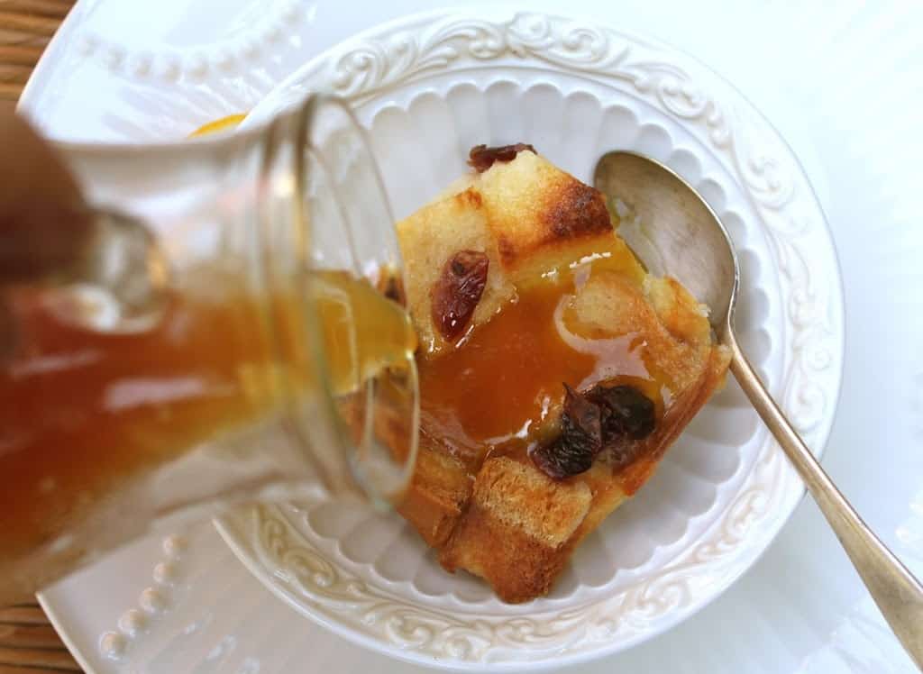 pouring sauce over orange cranberry bread pudding