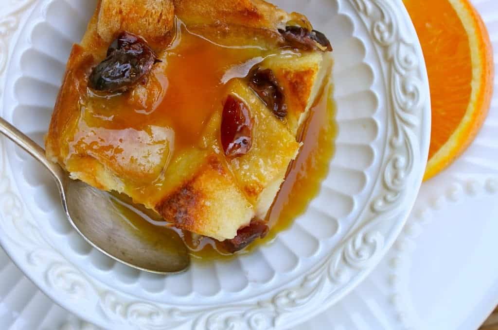 overhead view of cranberry orange bread pudding with a spoon and slice of orange