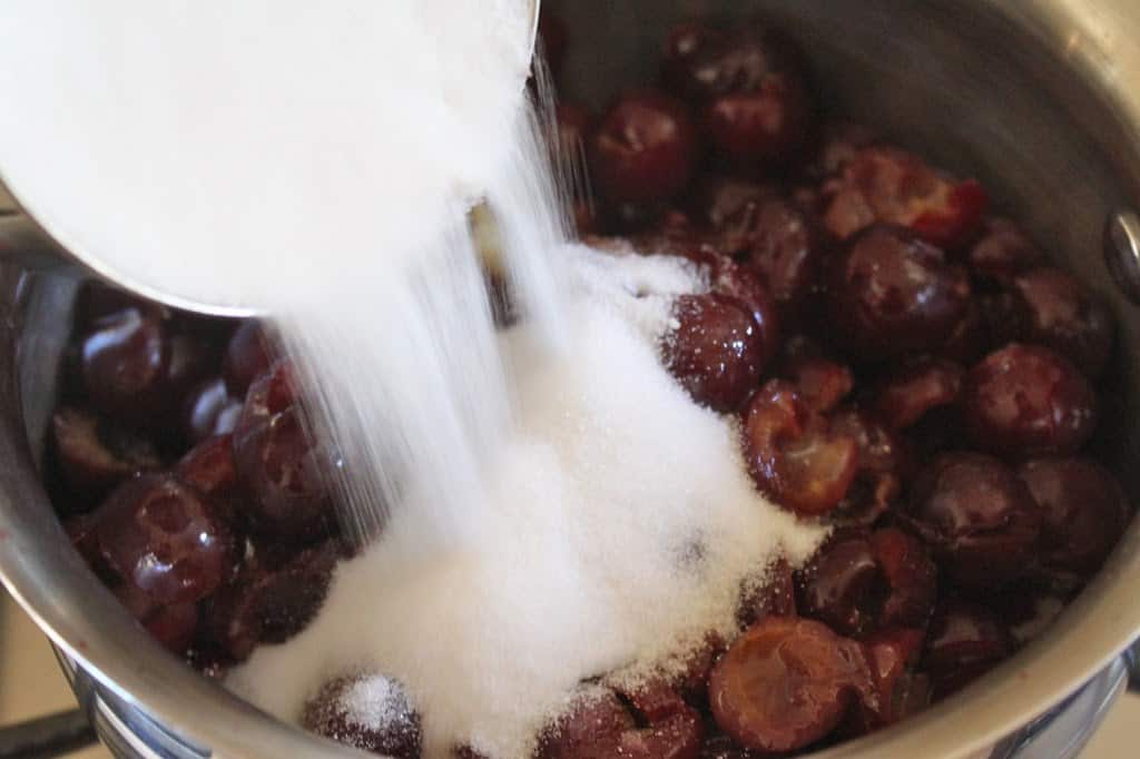 pouring sugar into cherries in pot