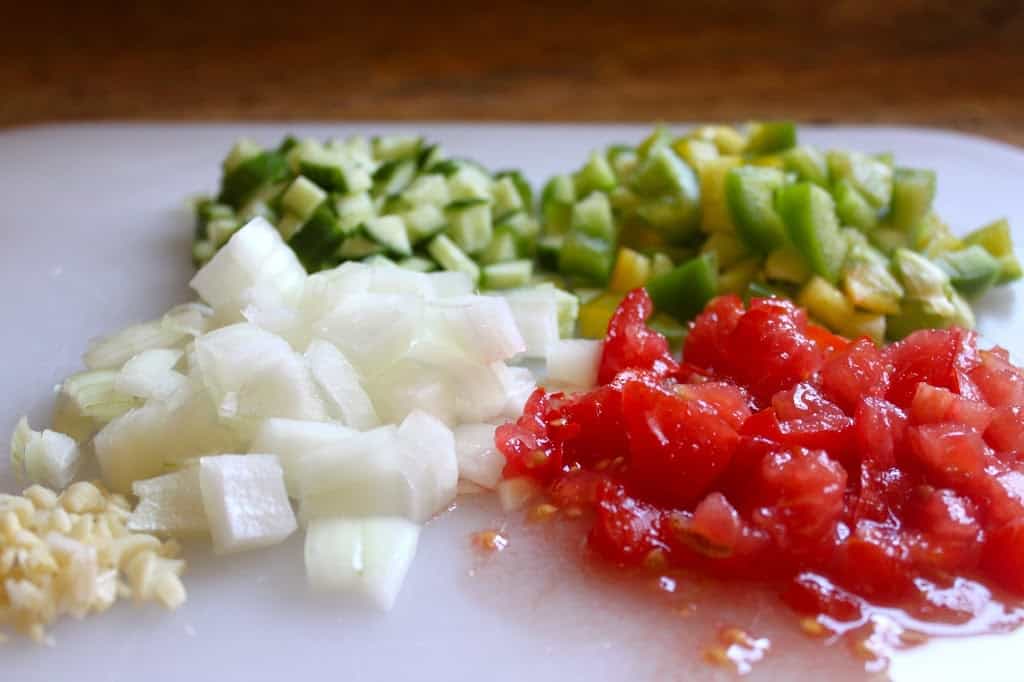 chopped onion, tomato, pepper, cucumber and garlic on a board