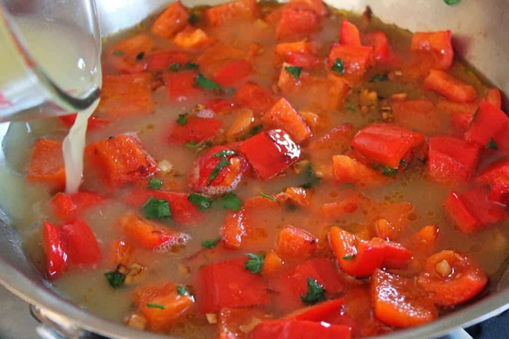 adding stock to red peppers in a pan