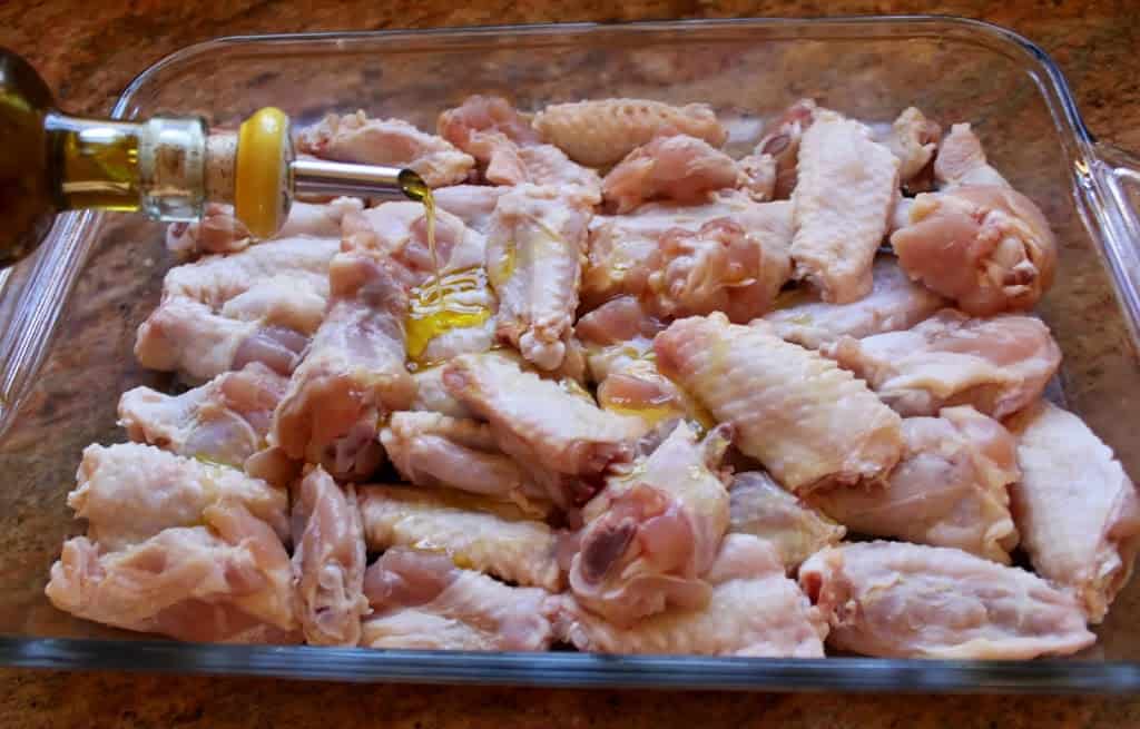 pouring oil onto chicken in a glass pan