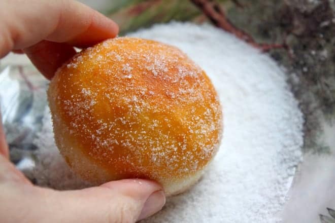 rolling circular doughnuts in sugar