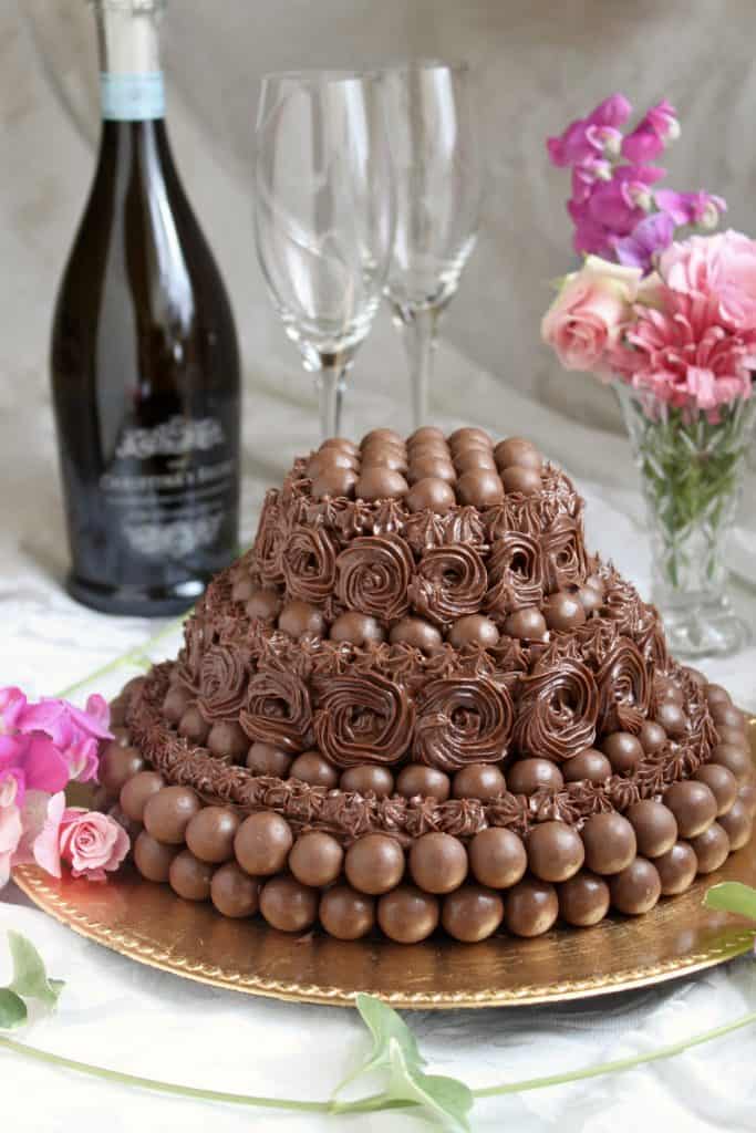 Malteser 3 tier cake with bottle of Prosecco and vase of flowers